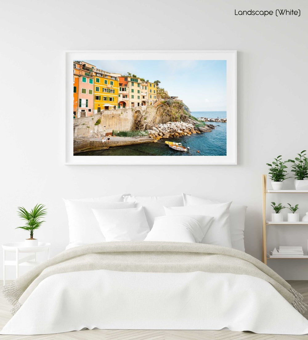 Man and woman sitting alongside docked boats and colorful buildings in Riomaggiore in a white fine art frame