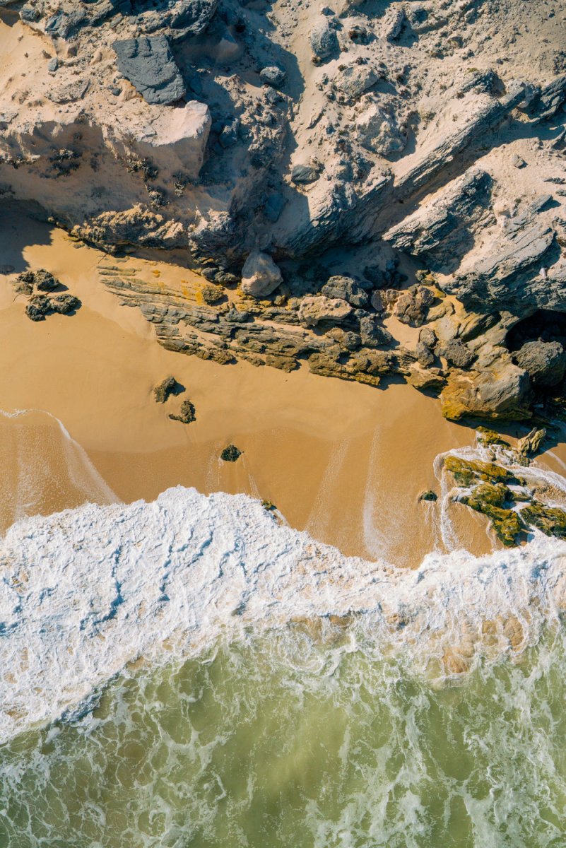 Waves crashing along the sand and up against a cliff of rocks in Cape Town.