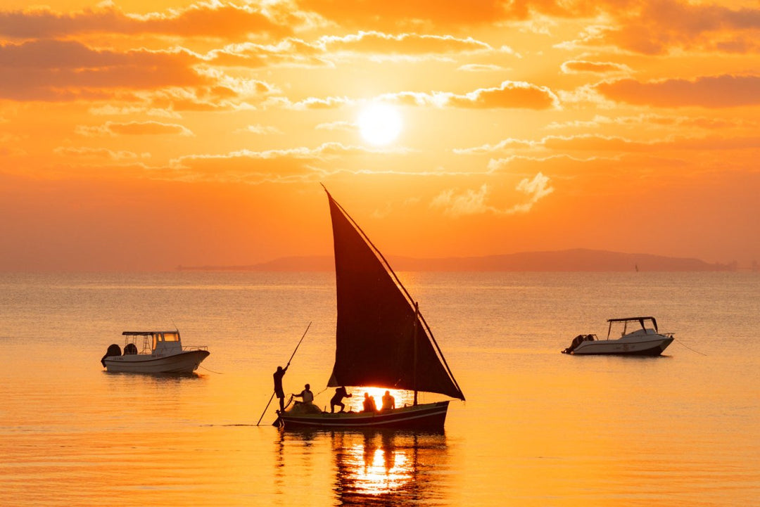 Orange sunrise with dhow boat and motor boats in Bazaruto Archipelago, Mozambique