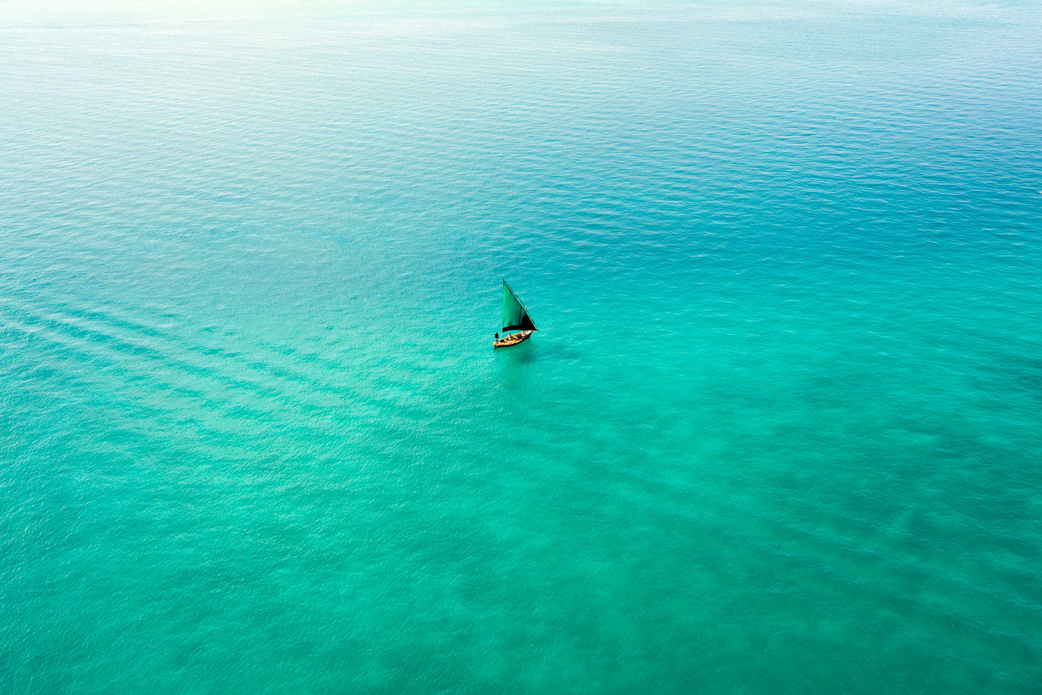 Aerial image taken from a helicopter flight of a dhow boat sailing in bright colourful indian ocean in Bazaruto Archipelago, Mozambique