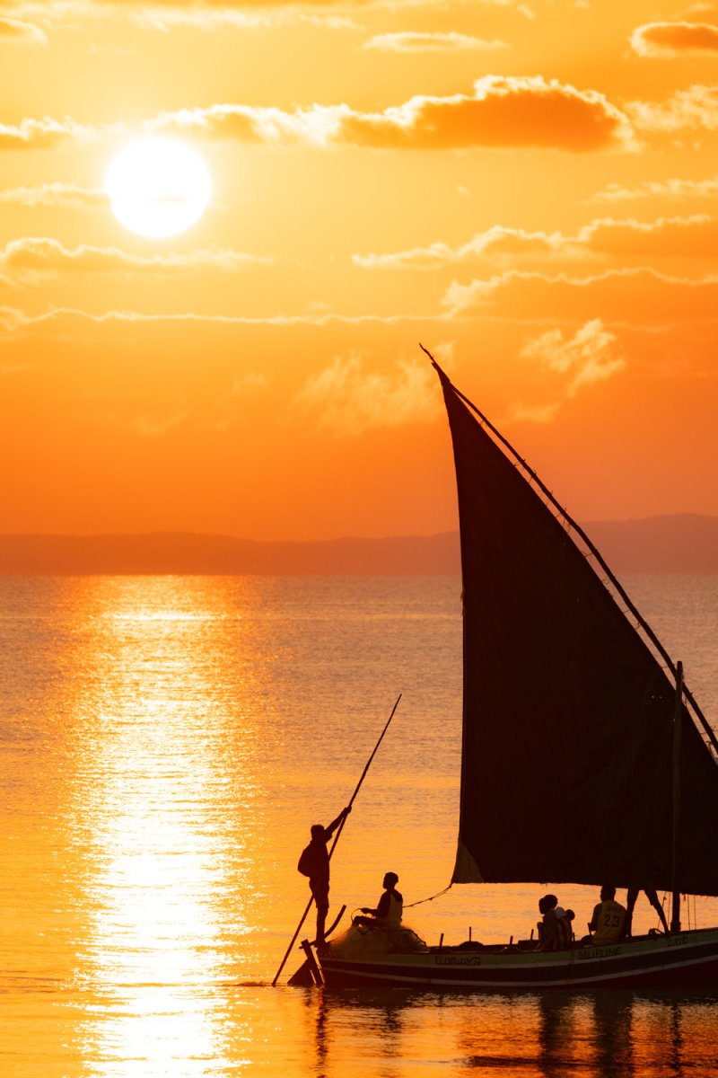 Orange image of dhow sailors passing by a big riding sun in the distance in Bazaruto Archipelago, Vilankulos, Mozambique