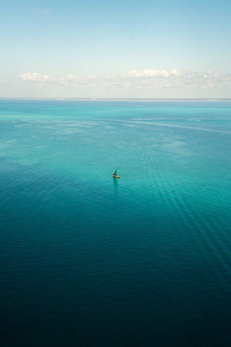 Aerial image of a single dhow boat sailing in the vast blue distance along calm sea in Bazaruto Archipelago, Vilankulos, Mozambique