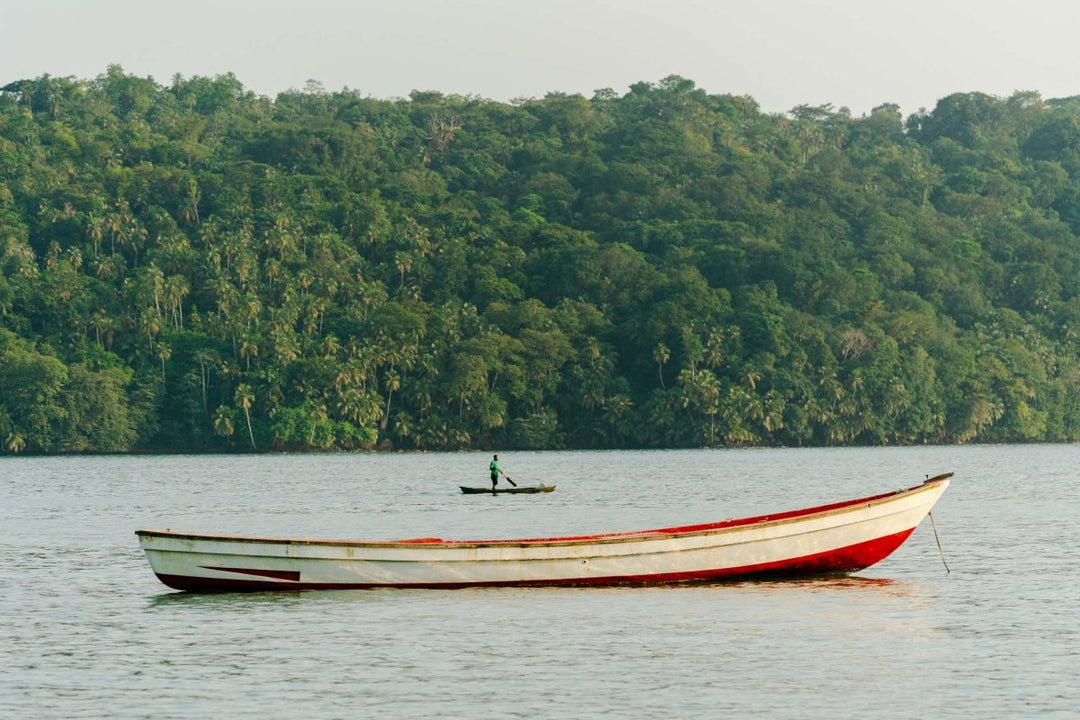 A man paddles on a canoe along tropical coastline of Sao Tome and Principe.