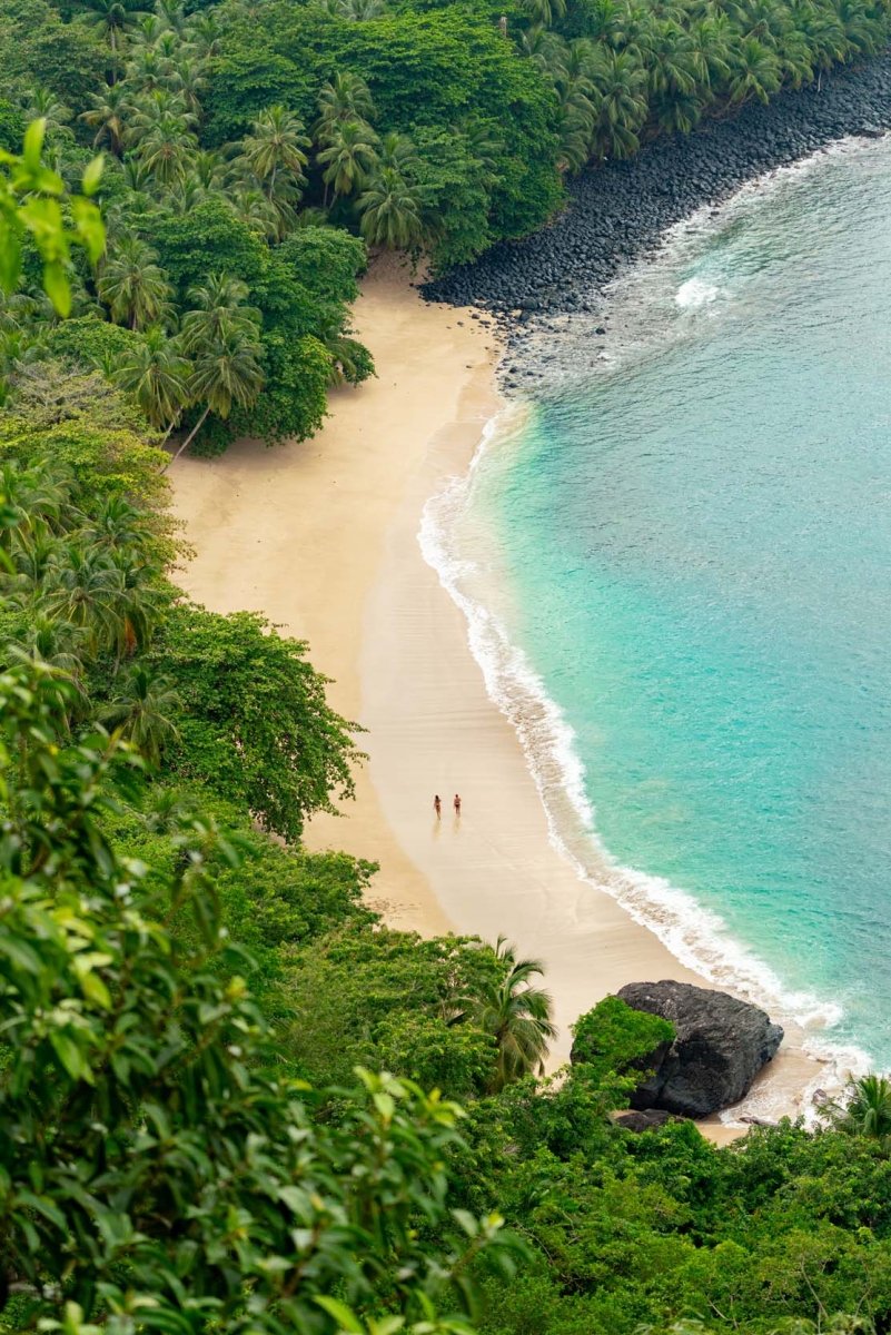 Two people on holiday walking along an empty beach on principe island