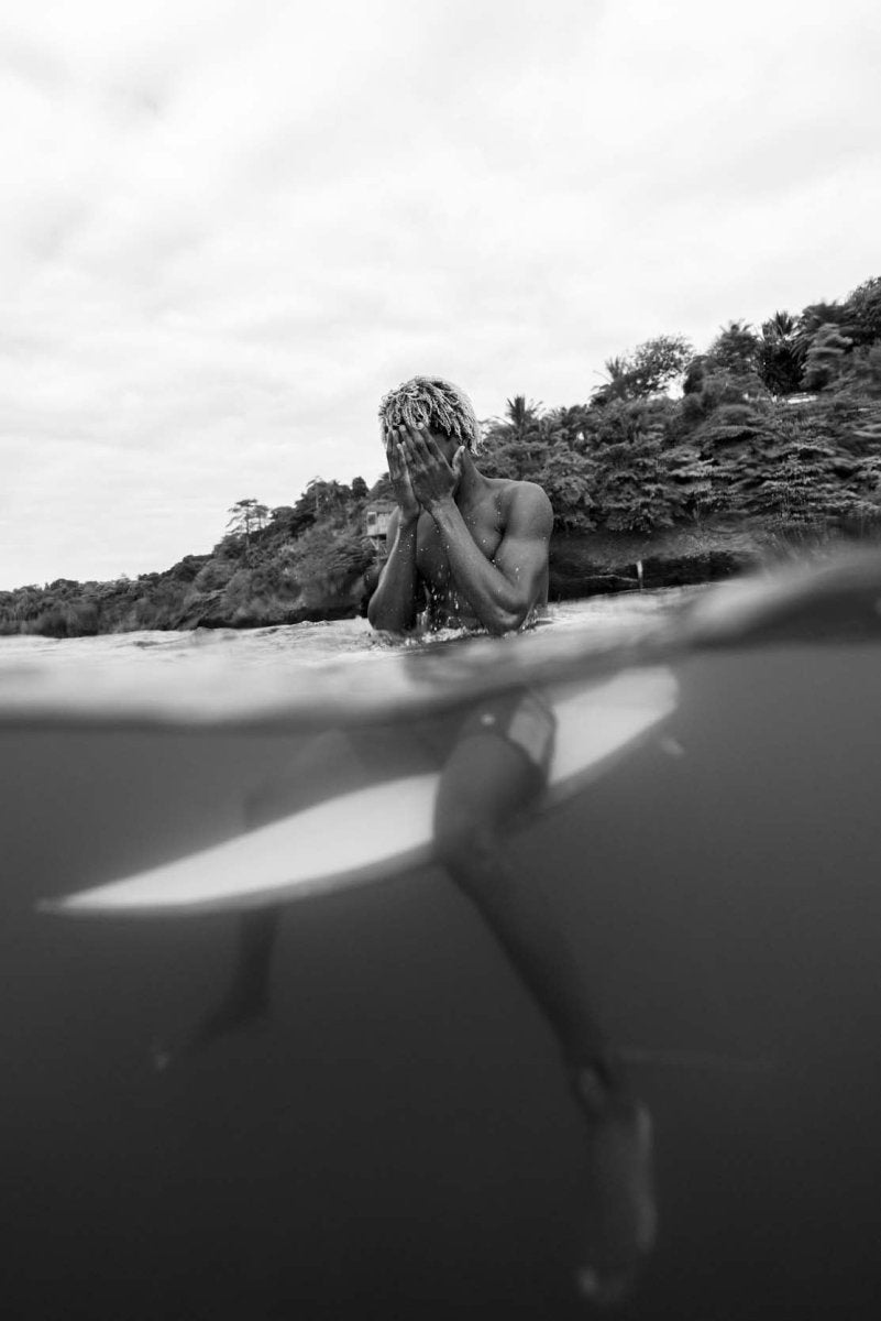 Surfer sitting on his board in the ocean while cleansing his face with the water