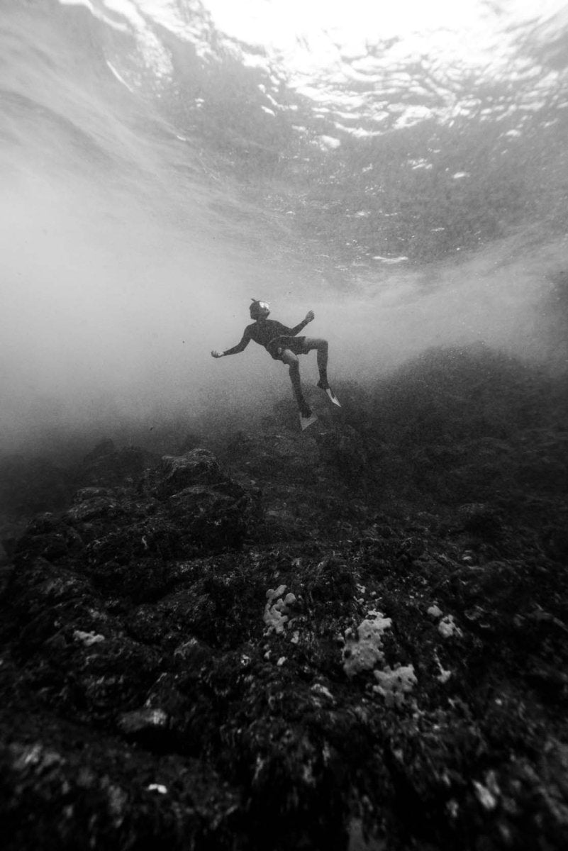 Man freediving underwater in clear water of principe island amidst volcanic rock formations and reef