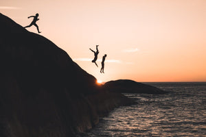 Three guys cliff jumping at sunset into ocean at Llandudno Beach