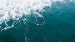 Aerial surfer paddling in dark ocean with foam