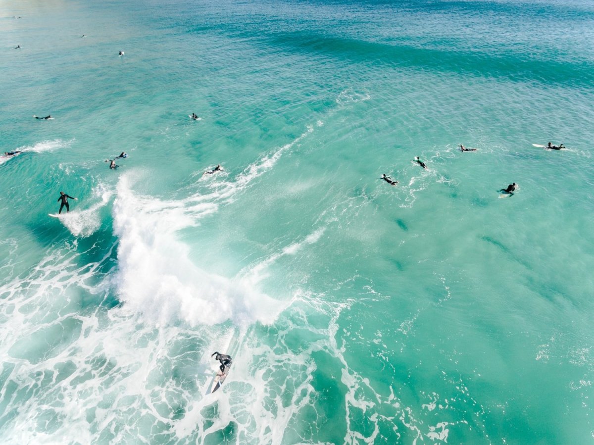 Aerial two surfers on one wave with other surfers paddling around blue swell in Cape Town