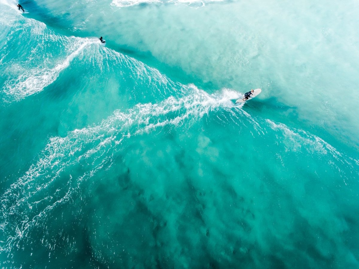 Three people surfing blue wave in Cape Town from above