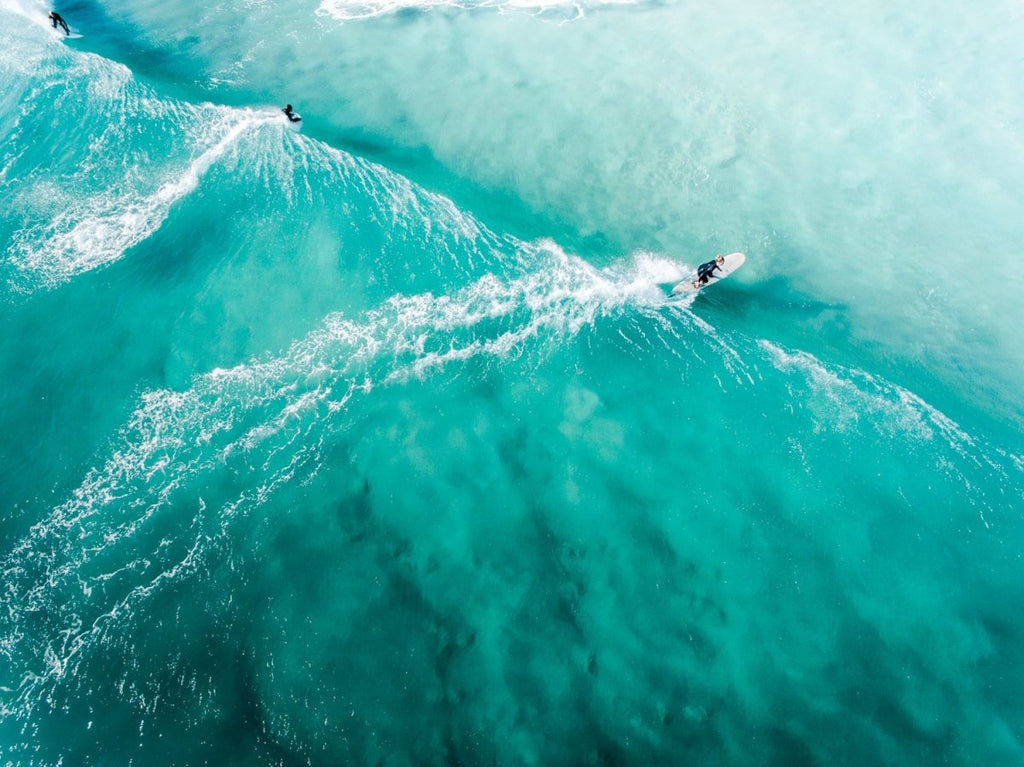 Three people surfing blue wave in Cape Town from above