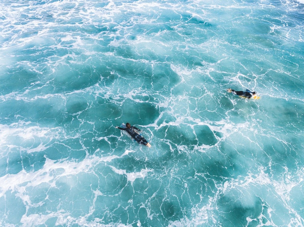 Aerial of two surfers paddling in foamy waves