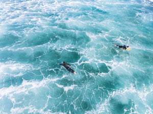 Aerial of two surfers paddling in foamy waves