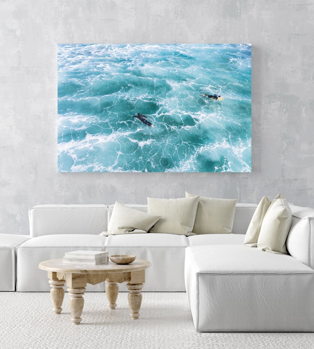 Aerial of two surfers paddling in foamy waves in an acrylic/perspex frame