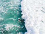 Aerial of one surfer paddling in on a foamy to Llandudno Beach