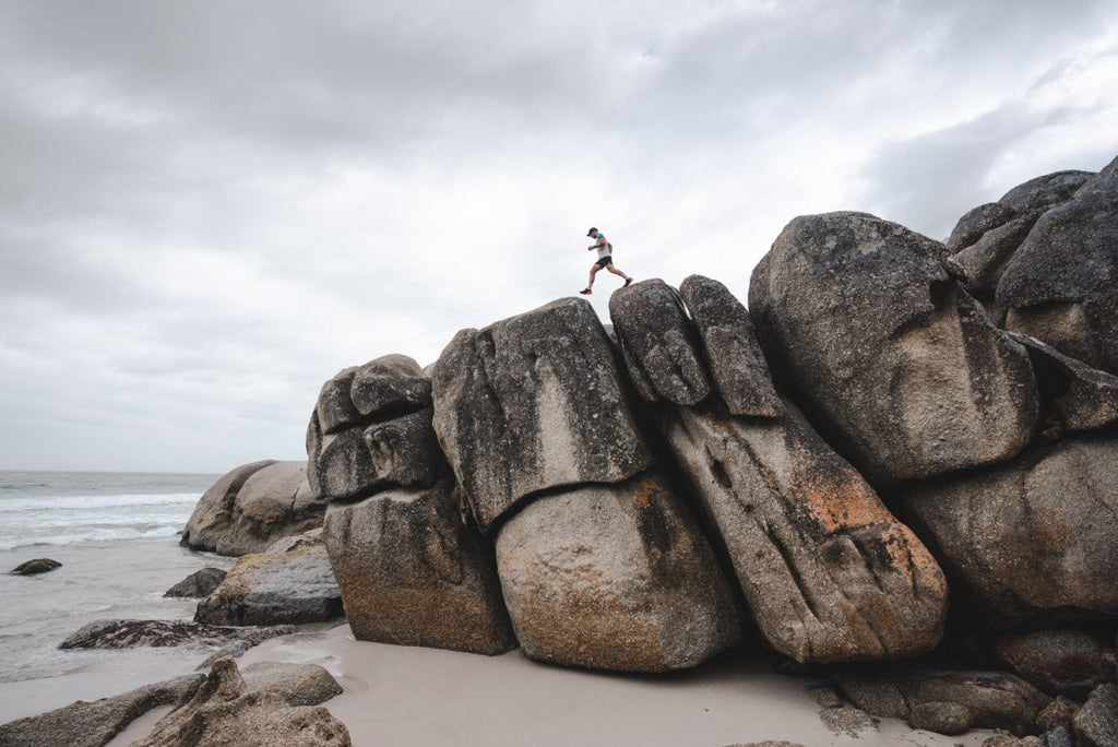 Man walking along high dark boulders on Cape Town beach