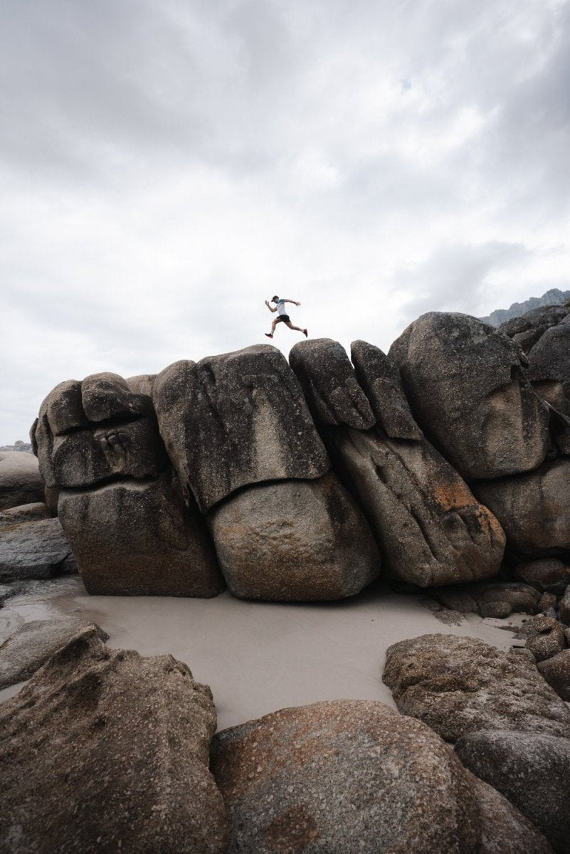 Man running along beach boulders on Llandudno beach in Cape Town