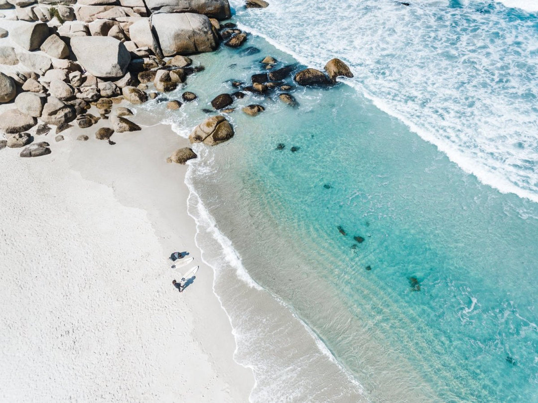 Aerial of two surfers about to get in blue water in Cape Town