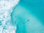 Aerial of surfer paddling in bright blue water in Cape Town