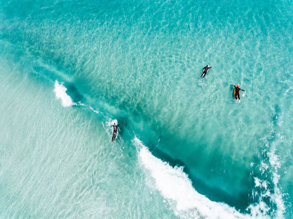 Aerial of surfers duckdiving blue wave at Glen Beach in Cape Town