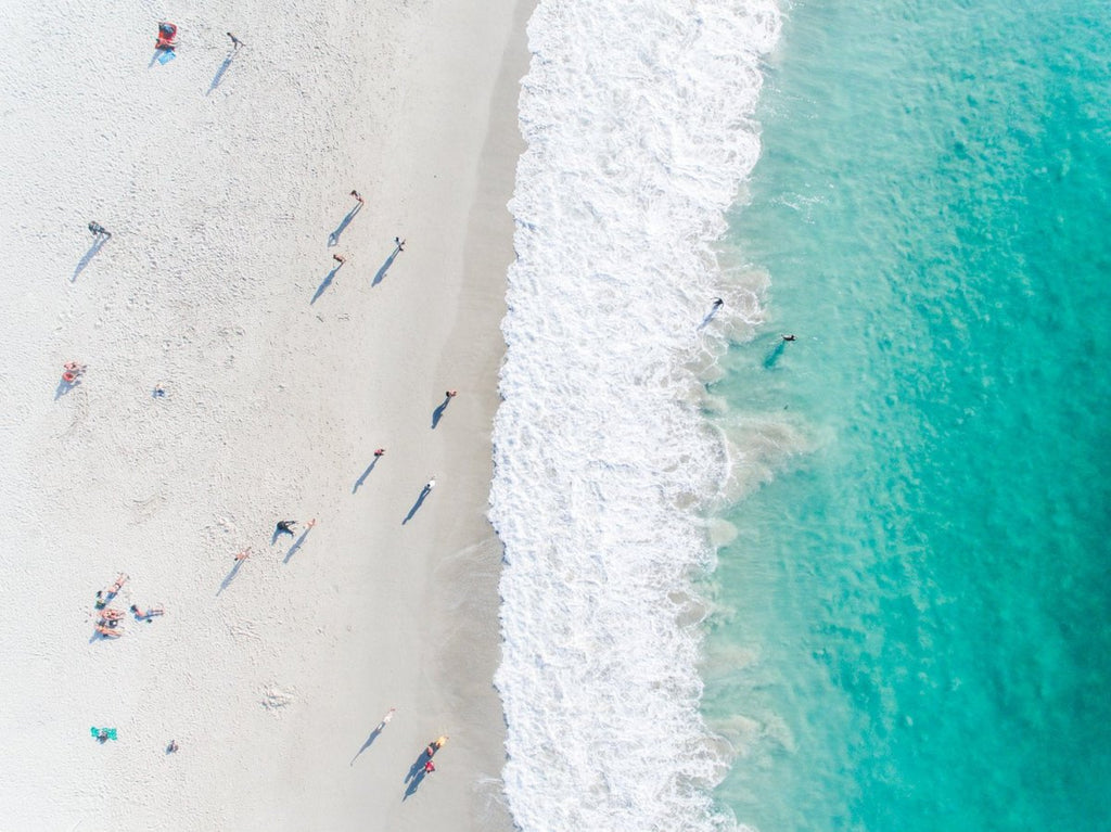 Aerial of green ocean at camps bay beach with people in cape town