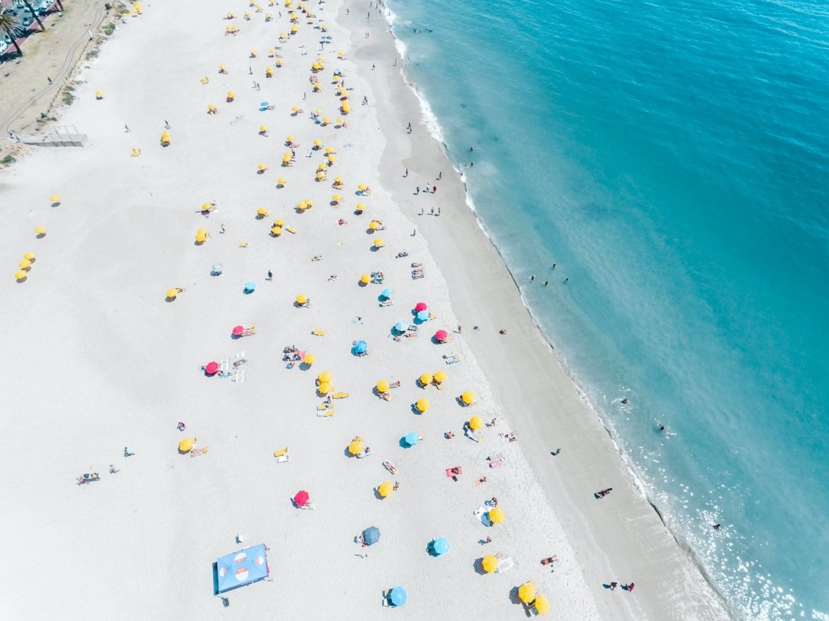 Aerial high above Camps Bay beach with lots of umbrellas and people