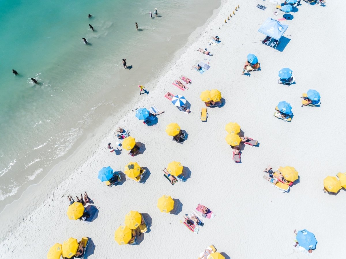 Aerial of green sea and colorful umbrellas from above on Camps Bay beach