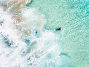 Aerial view of two surfers paddling in turquoise water and foam