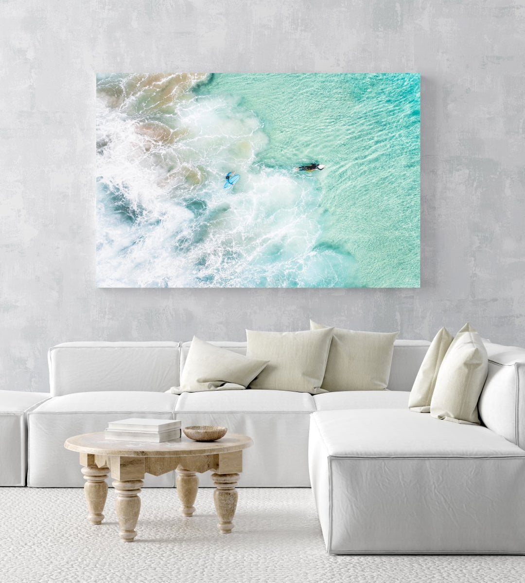 Aerial view of two surfers paddling in turquoise water and foam in a white fine art frame