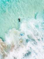 Aerial view of two surfers paddling in turquoise water and foam