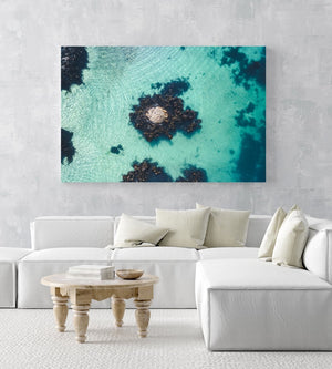One rock with seaweed in middle of blue green water from above in a white fine art frame