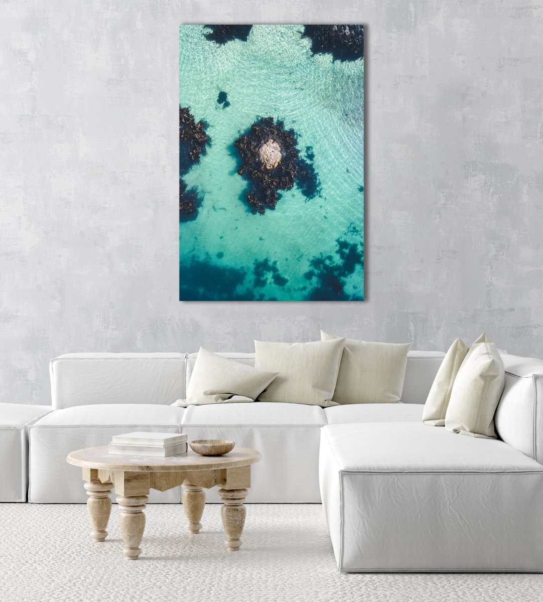 One rock with seaweed in middle of blue green water from above in a natural fine art frame