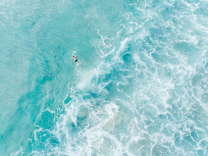 Light blue surfer paddling through foam from above