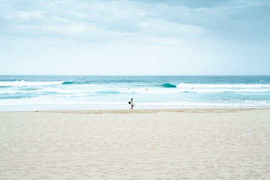 Man with surfboard looking out to blue waves along Manly Beach in Sydney