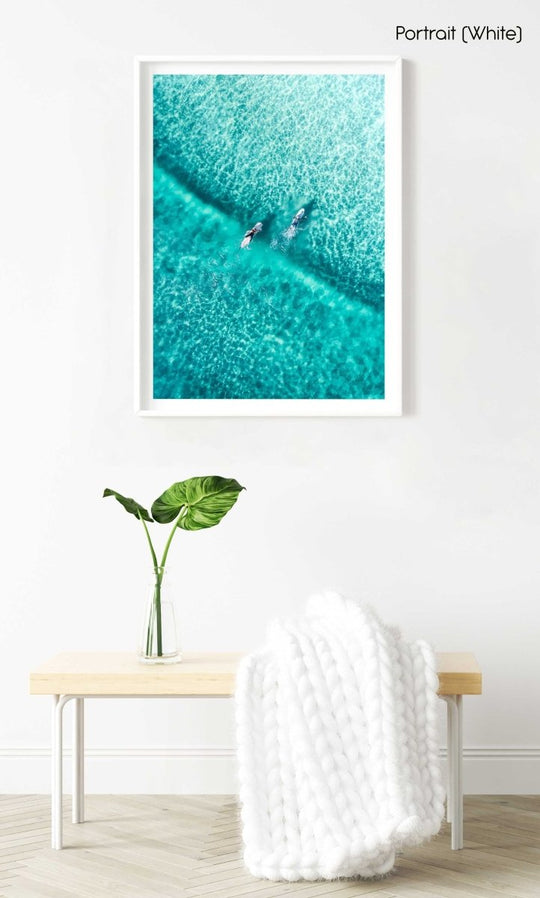 Two surfers paddling on one blue wave from aerial view in a white fine art frame