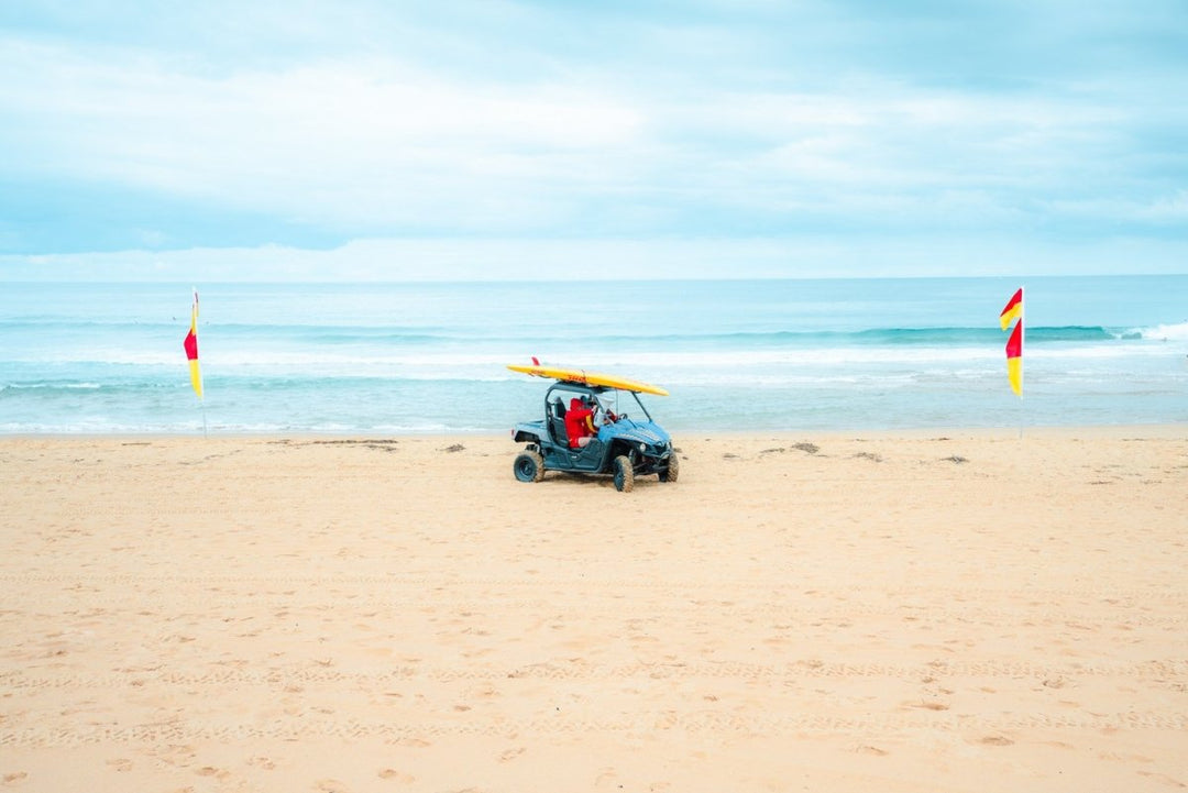 Lifesavers in a blue beach buggy with yellow board on roof in Monavale Beach Sydney