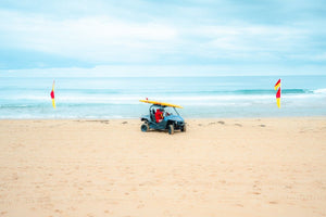 Lifesavers in a blue beach buggy with yellow board on roof in Monavale Beach Sydney