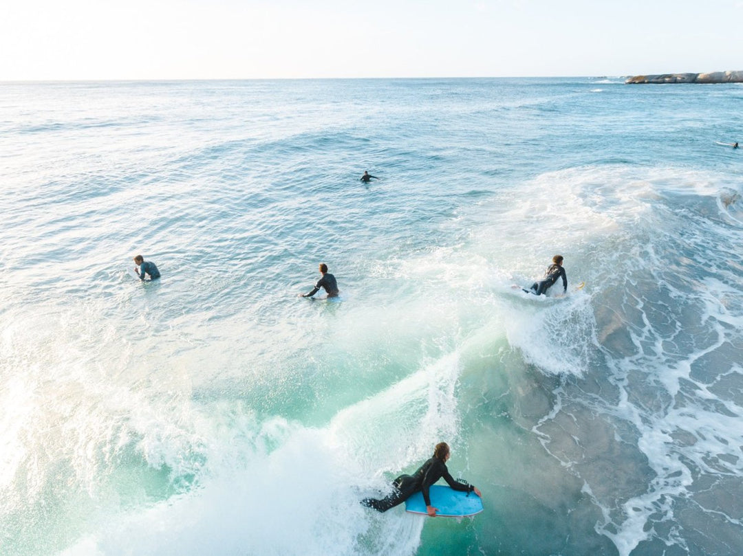 Aerial of bodyboarder surfing a wave amongst other surfers in Sandy Bay Cape Town