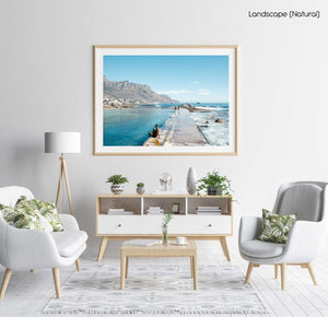 Man sitting along edge of Camps Bay pool with twelve apostles mountains in background in a natural fine art frame