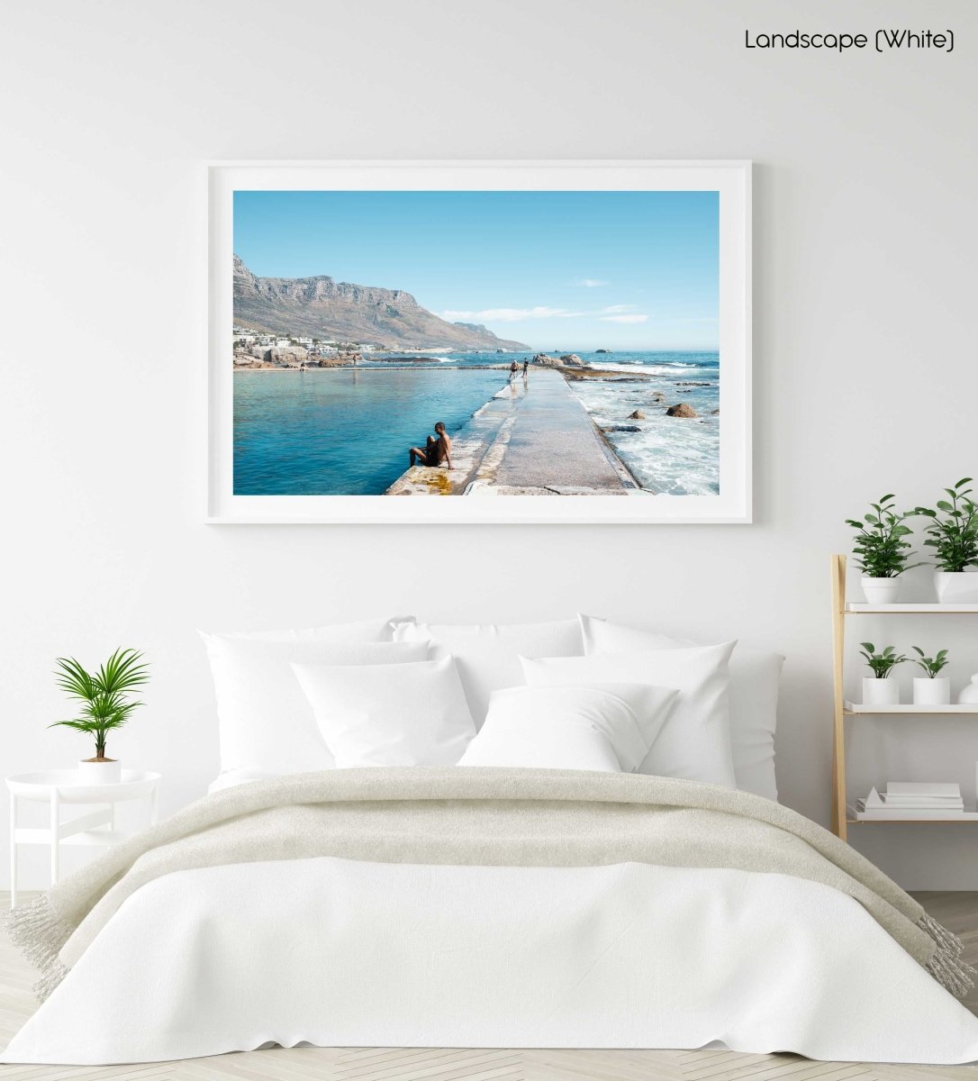 Man sitting along edge of Camps Bay pool with twelve apostles mountains in background in a white fine art frame
