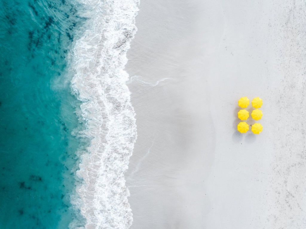 Aerial of six yellow umbrellas next to blue ocean on Camps Bay beach in Cape Town