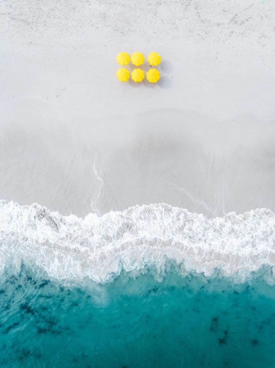 Aerial of six yellow umbrellas next to blue ocean on Camps Bay beach in Cape Town