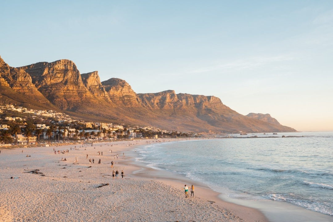 People walking along Camps Bay beach during an orange sunset