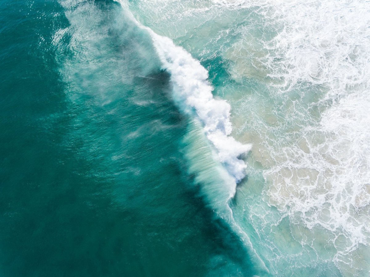 Big wave breaking in dark turquoise Noordhoek Beach from the air