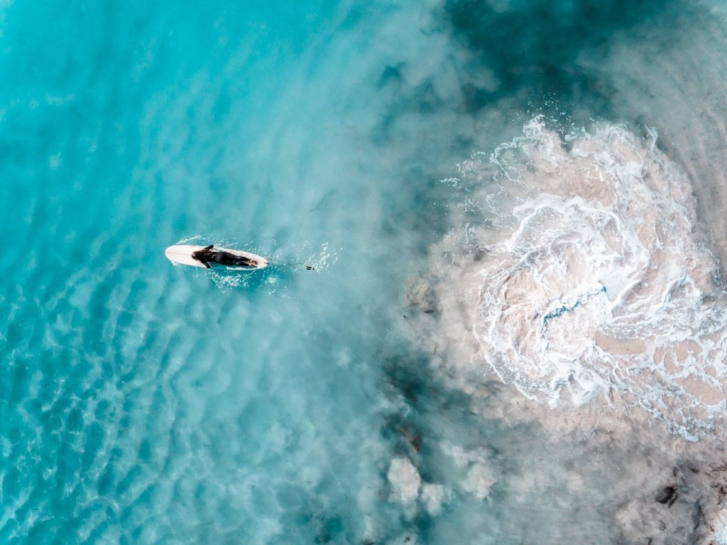 Aerial topdown of girl surfer in wetsuit paddling in blue water
