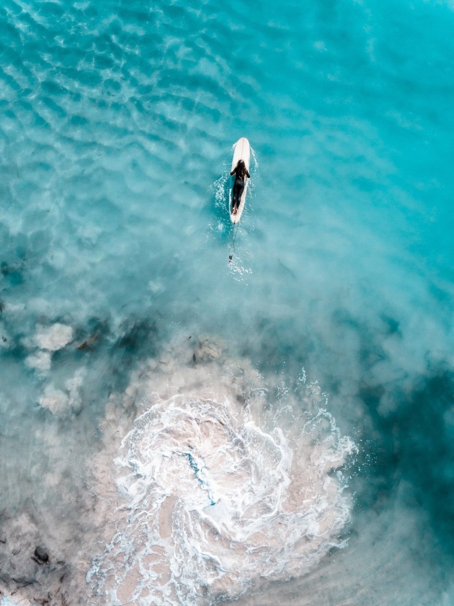 Aerial topdown of girl surfer in wetsuit paddling in blue water