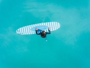 Aerial of girl holding striped surfboard in blue water in Camps Bay Beach