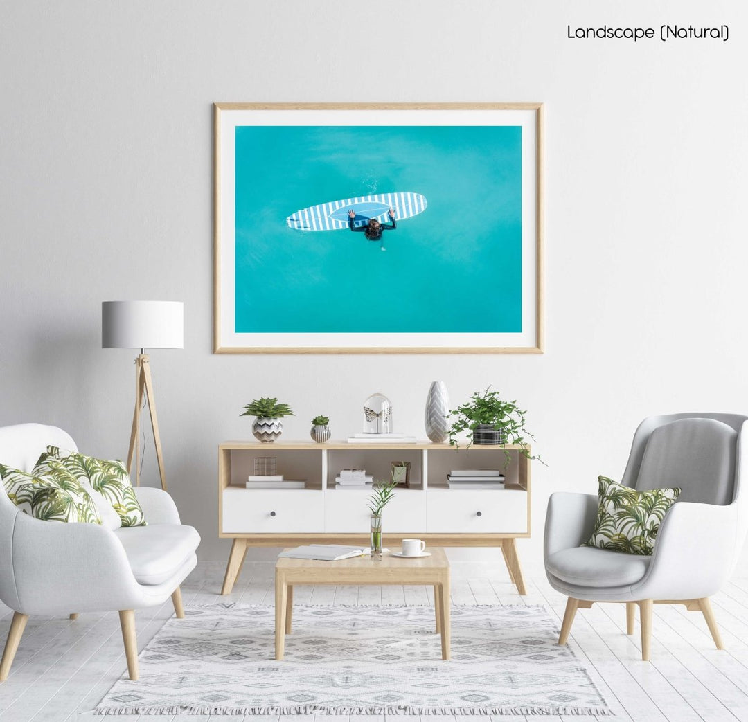 Aerial of girl holding striped surfboard in blue water in Camps Bay Beach in a natural fine art frame