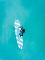Aerial of girl holding striped surfboard in blue water in Camps Bay Beach