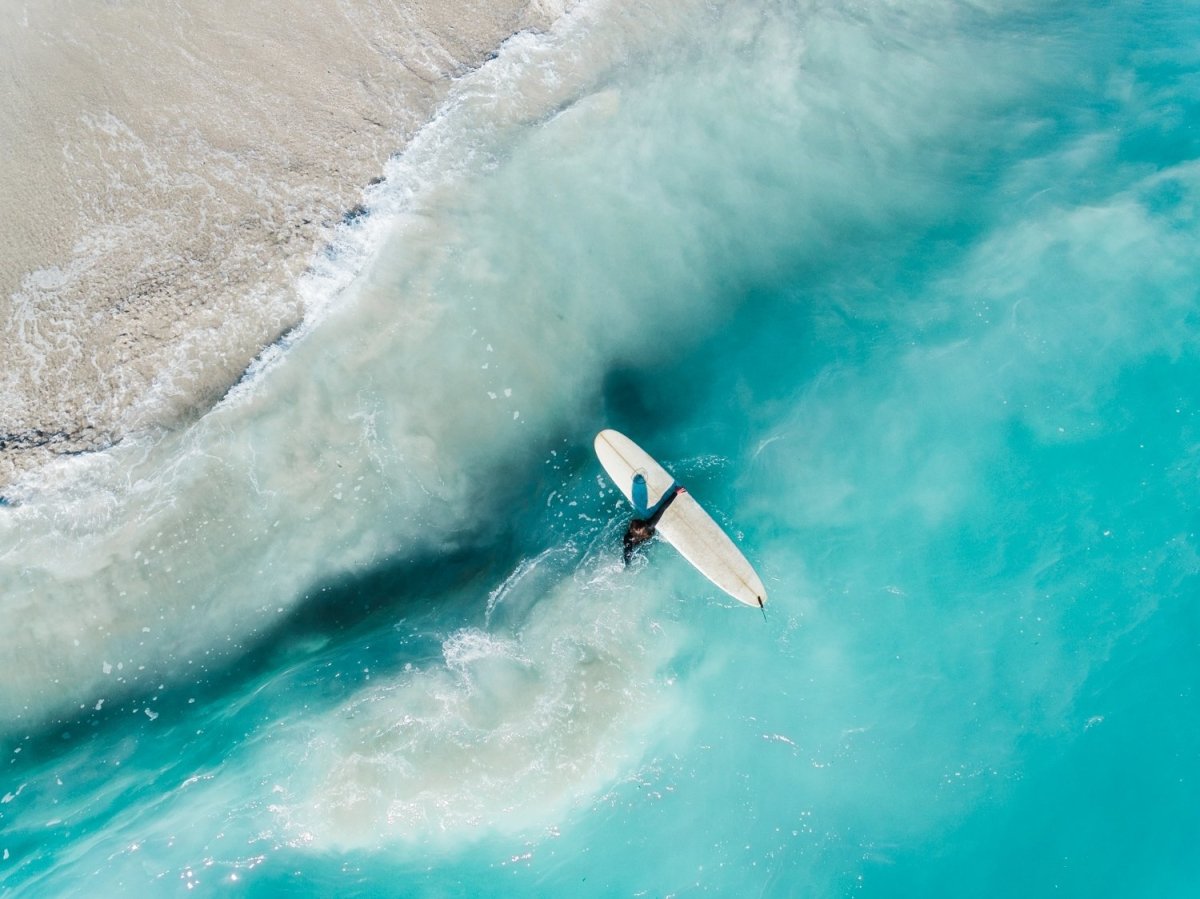 Girl walking back to shore with surfboard in blue water and waves